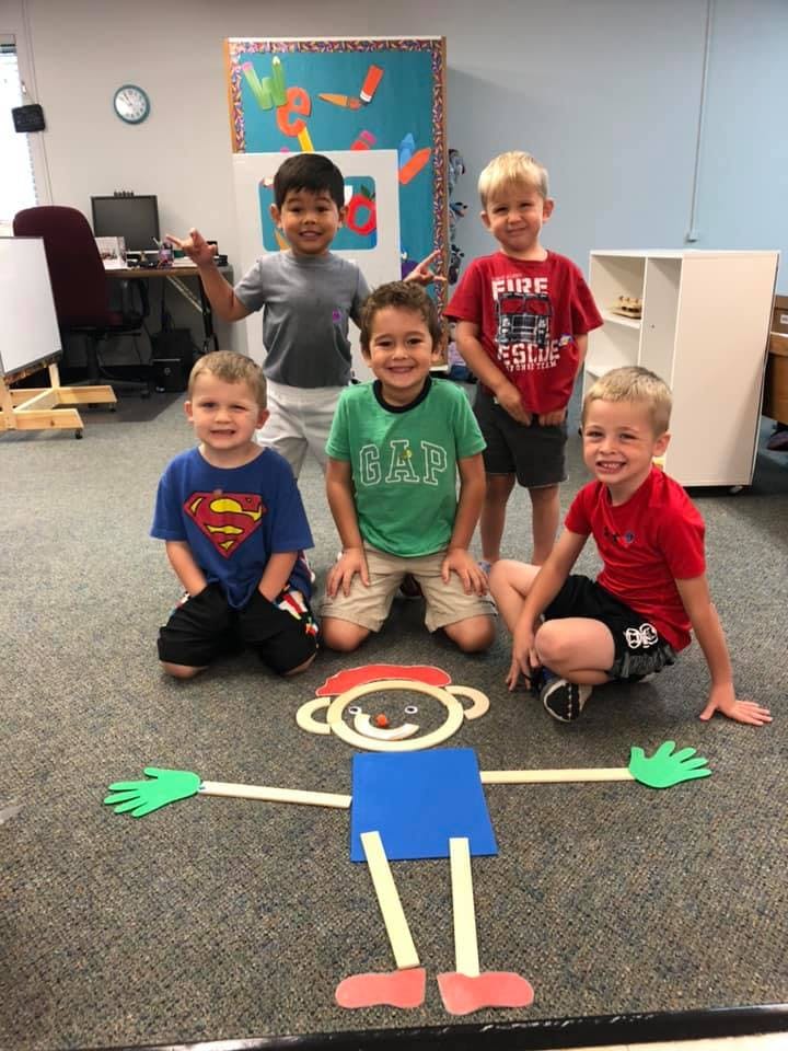 Five children posing around a craft person on the floor in a classroom