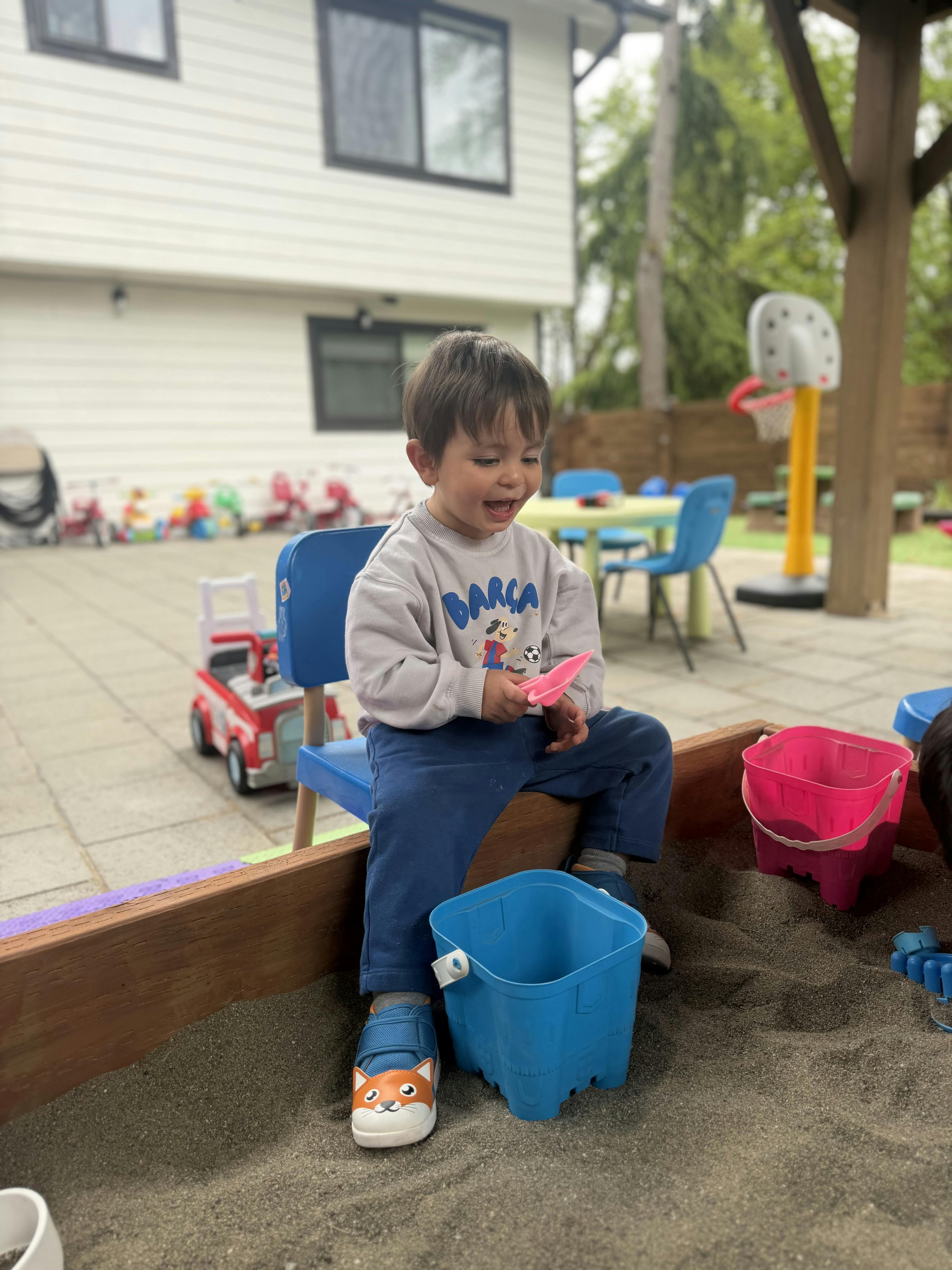 Child sitting on a chair in a sandbox, holding a pink shovel