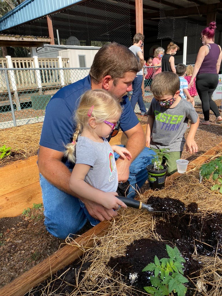 Adult and two children planting in a garden bed