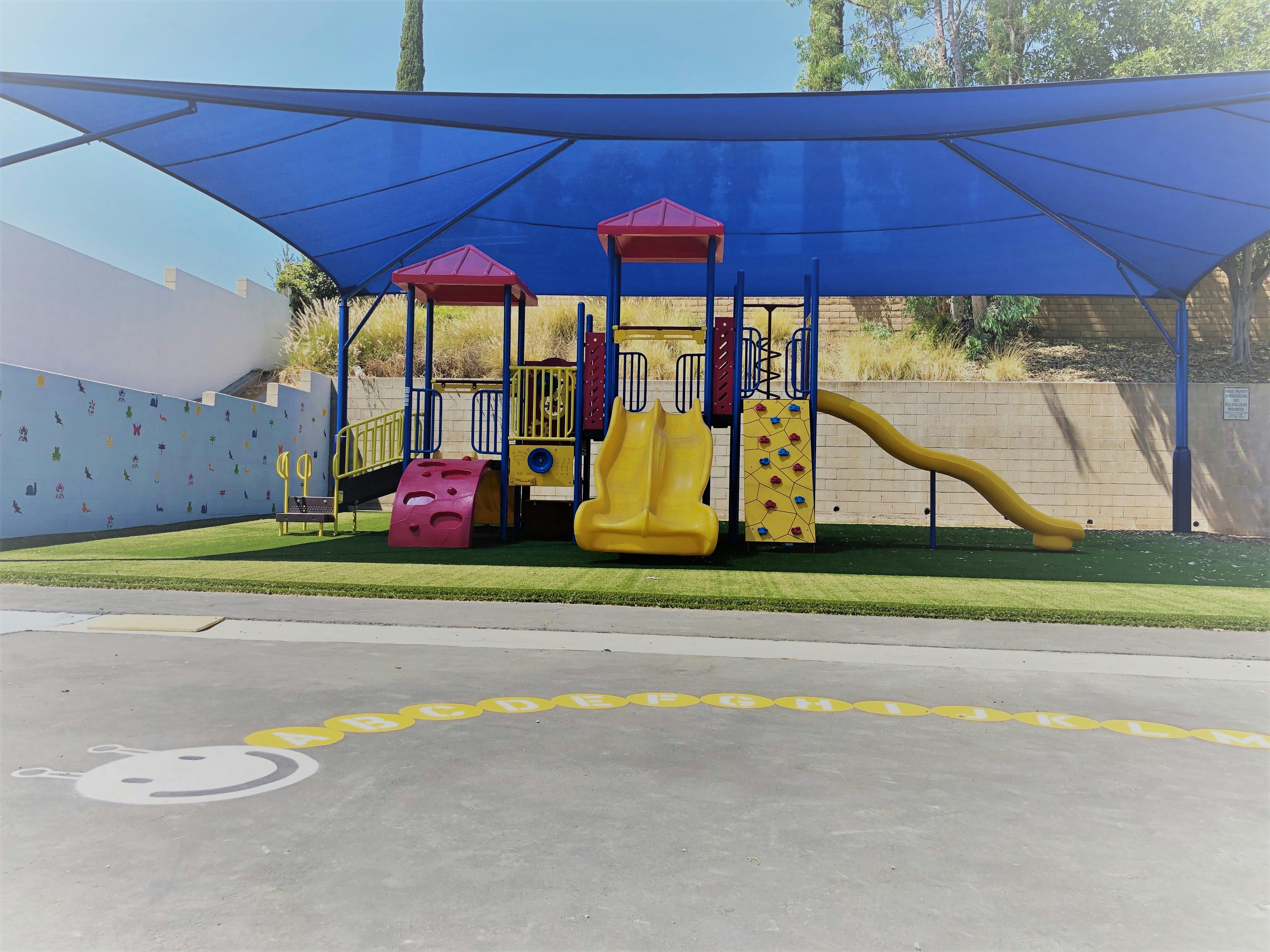Playground with slides and climbing structures under a blue shade sail