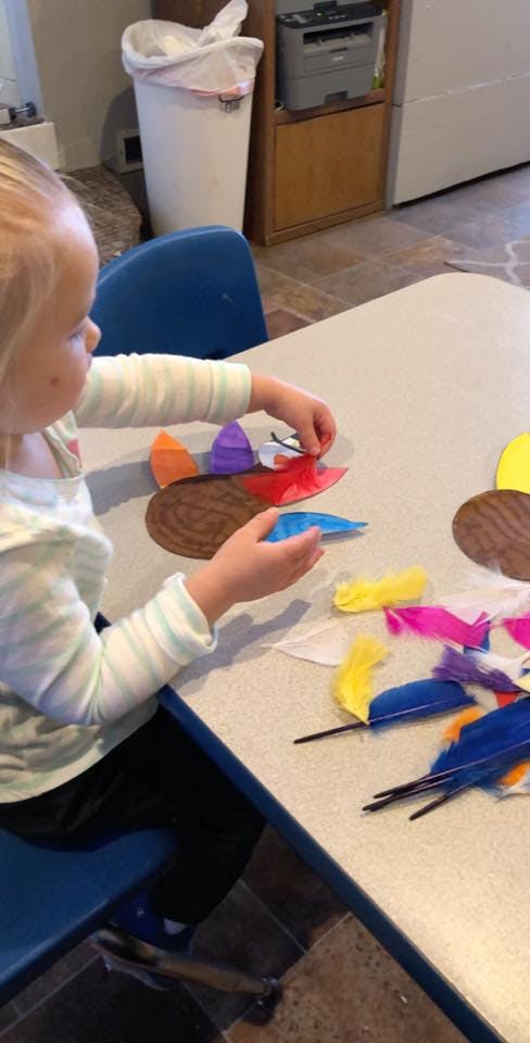 Child making a craft with paper cutouts and colorful feathers