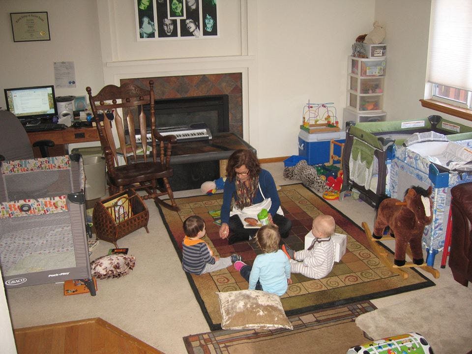 Person reading to three children in a room with cribs and toys