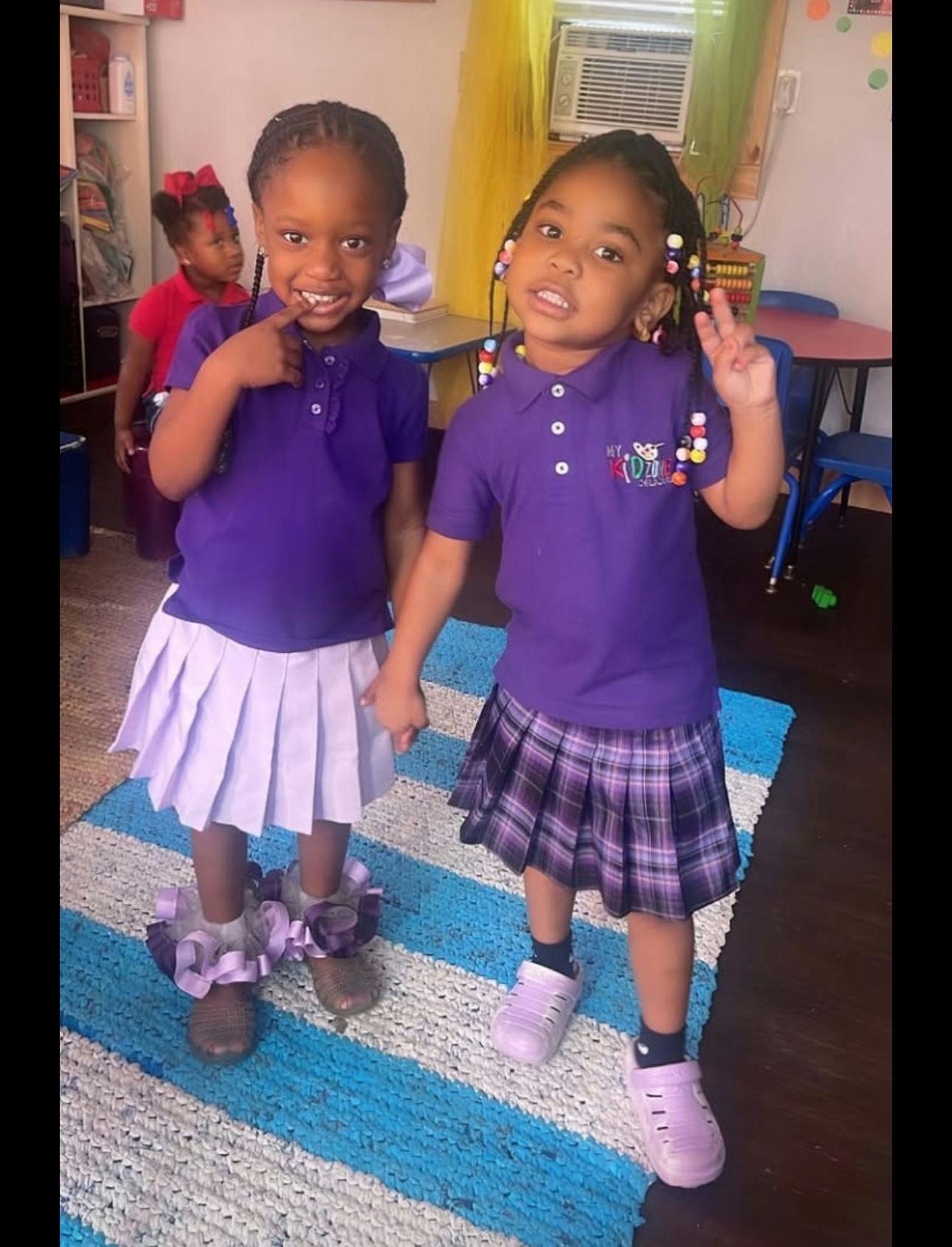 Two children in purple shirts and skirts standing on a striped rug