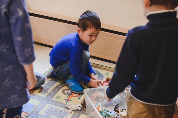 Child kneeling on a rug, playing with toys from a clear bin