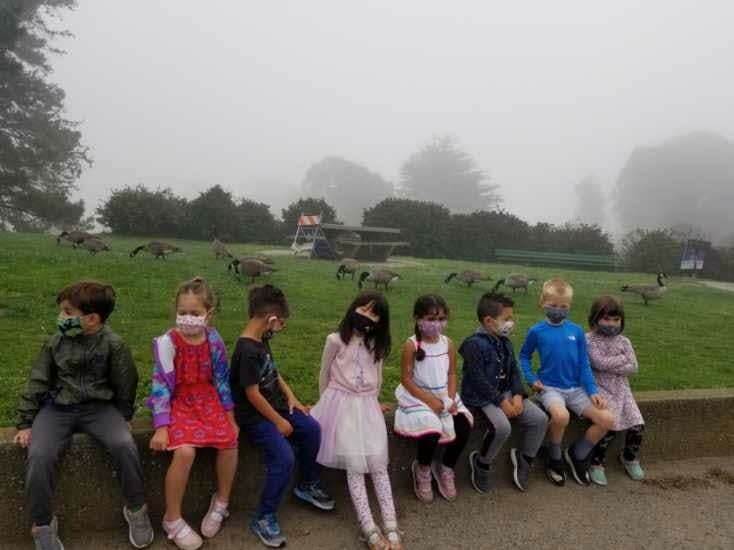 Group of children wearing masks sitting outdoors