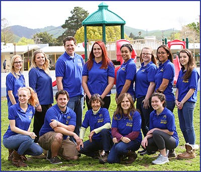 Group of people in blue shirts posing outdoors near a playground