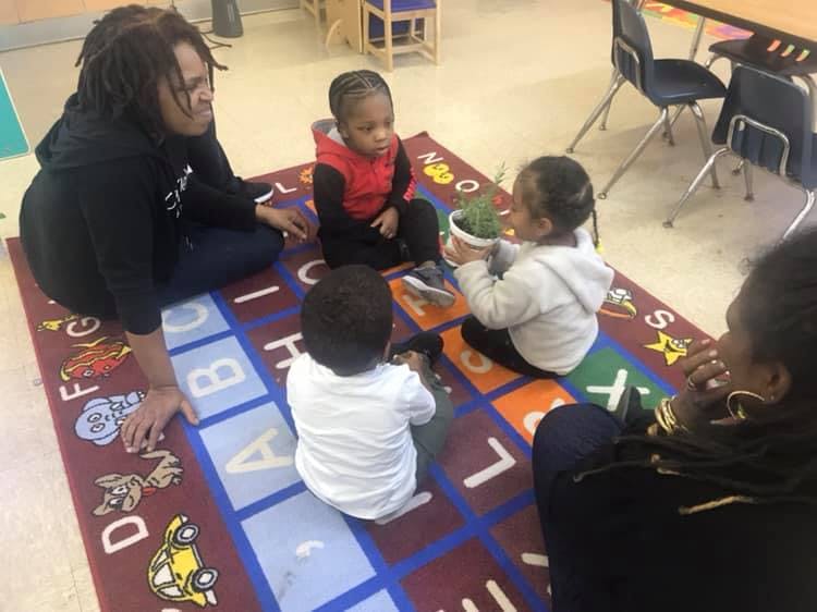 Two adults and three children sitting on an alphabet rug