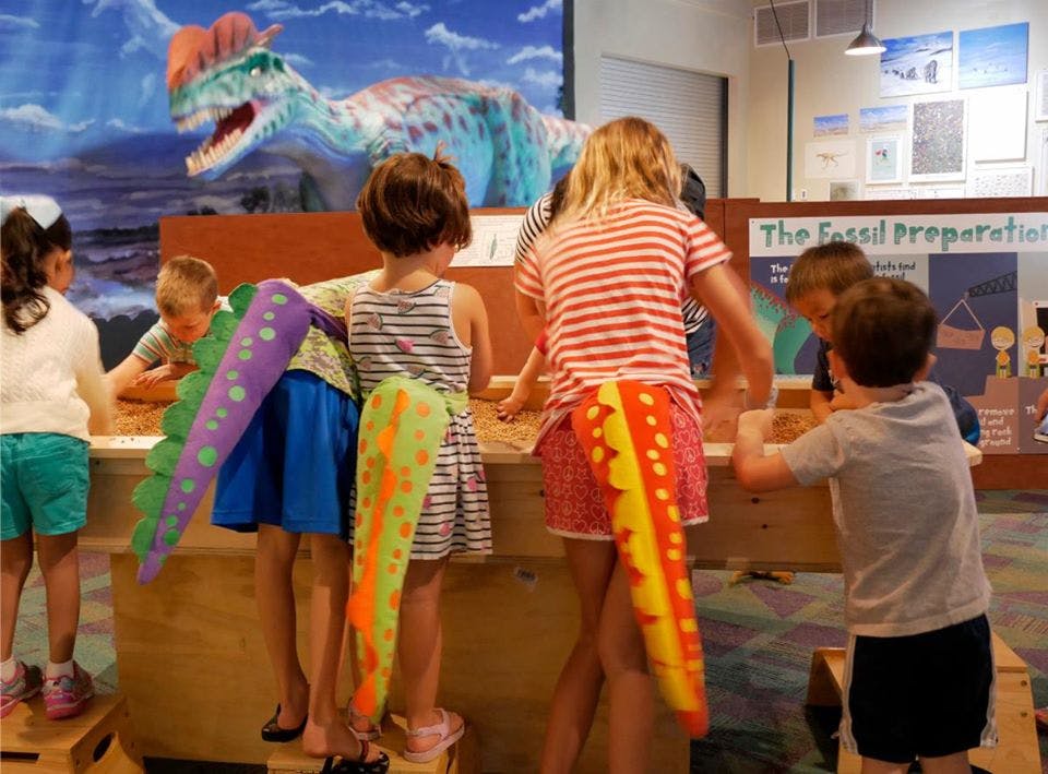 Children playing in a room with a large dinosaur model in the background