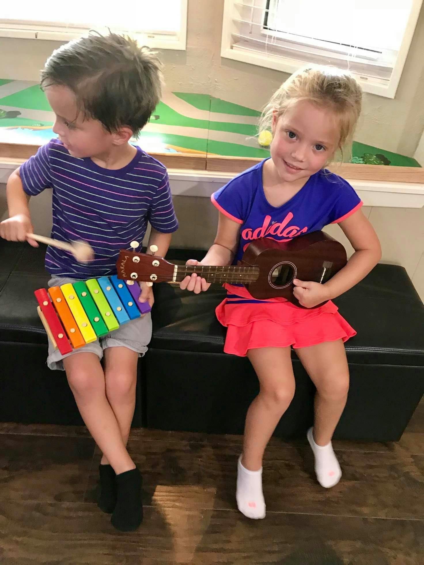 Two children playing musical instruments, one with a xylophone, one with a ukulele