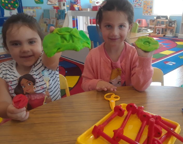 Two children at a table holding green playdough