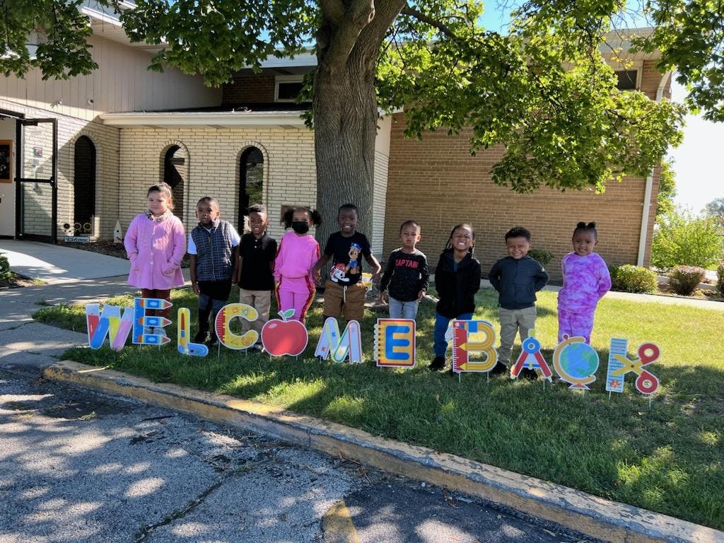 Group of children standing behind a "Welcome Back" sign