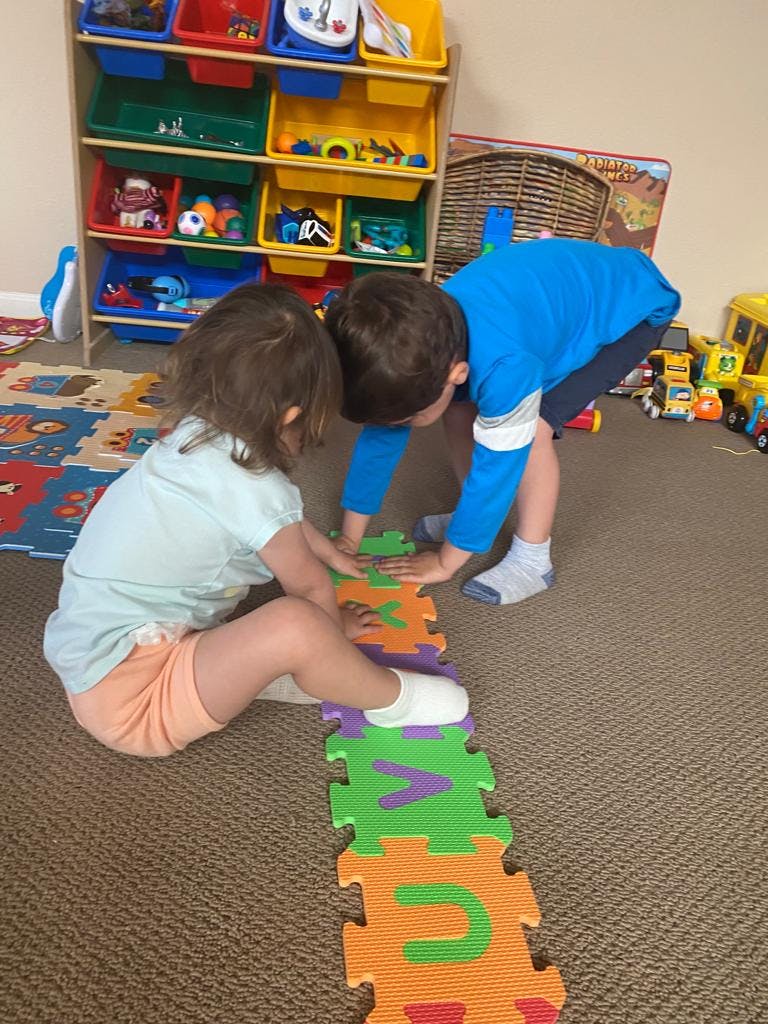 Two children playing with alphabet puzzle mats on the floor