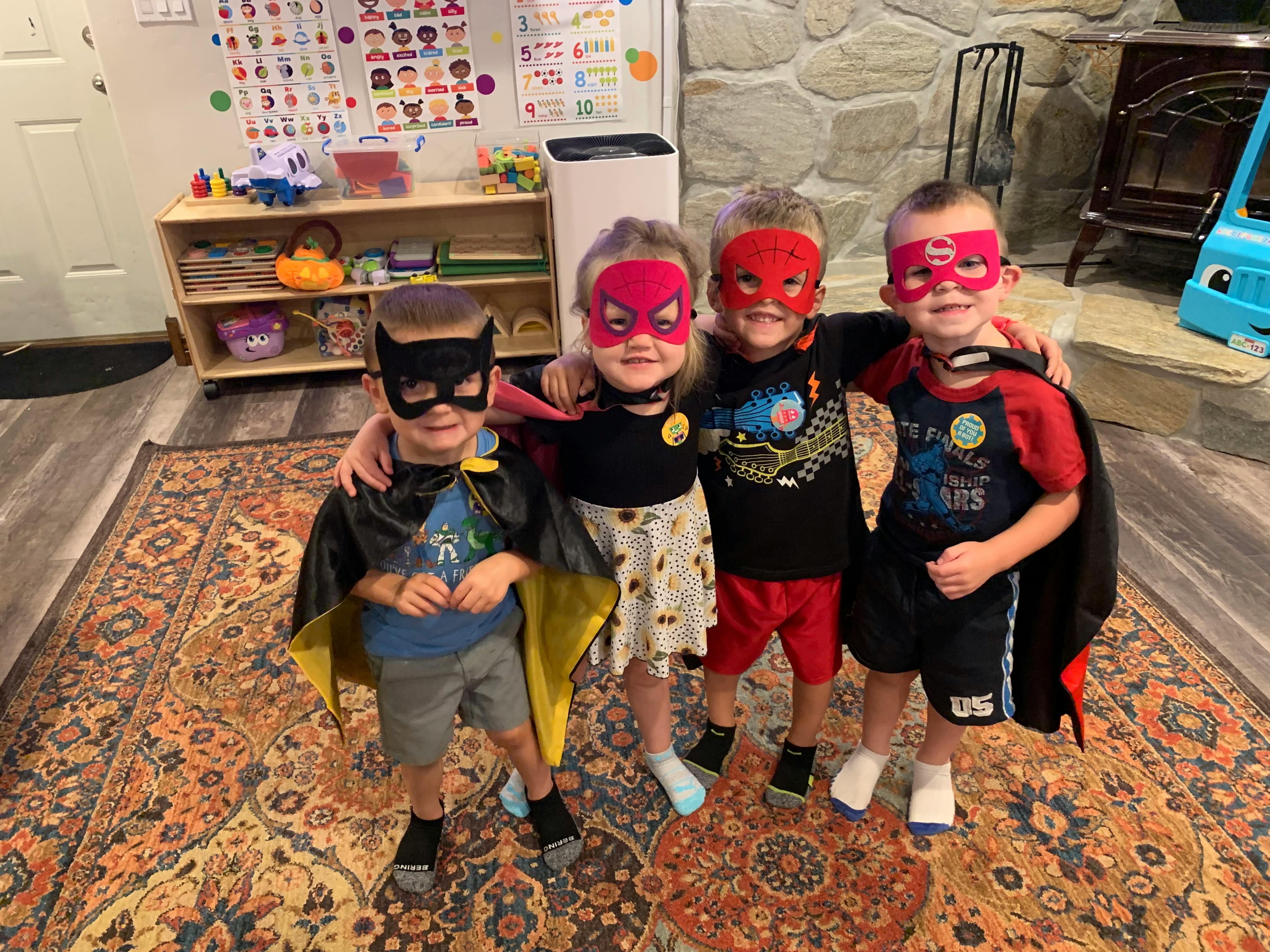 Four children in superhero masks and capes standing together