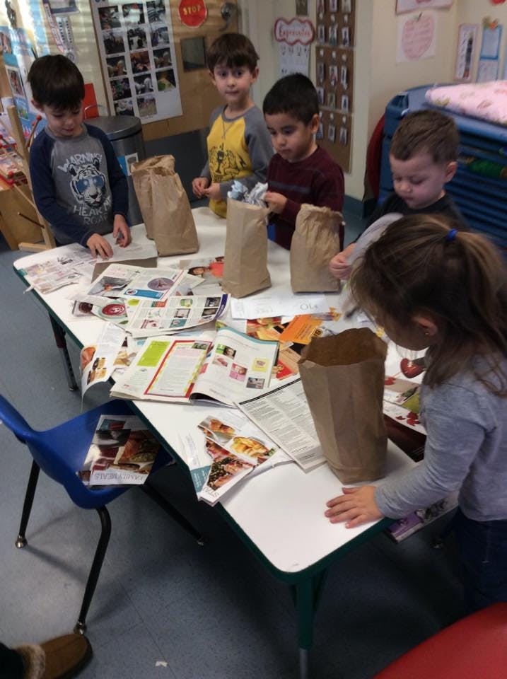 Children at a table with open books and paper bags