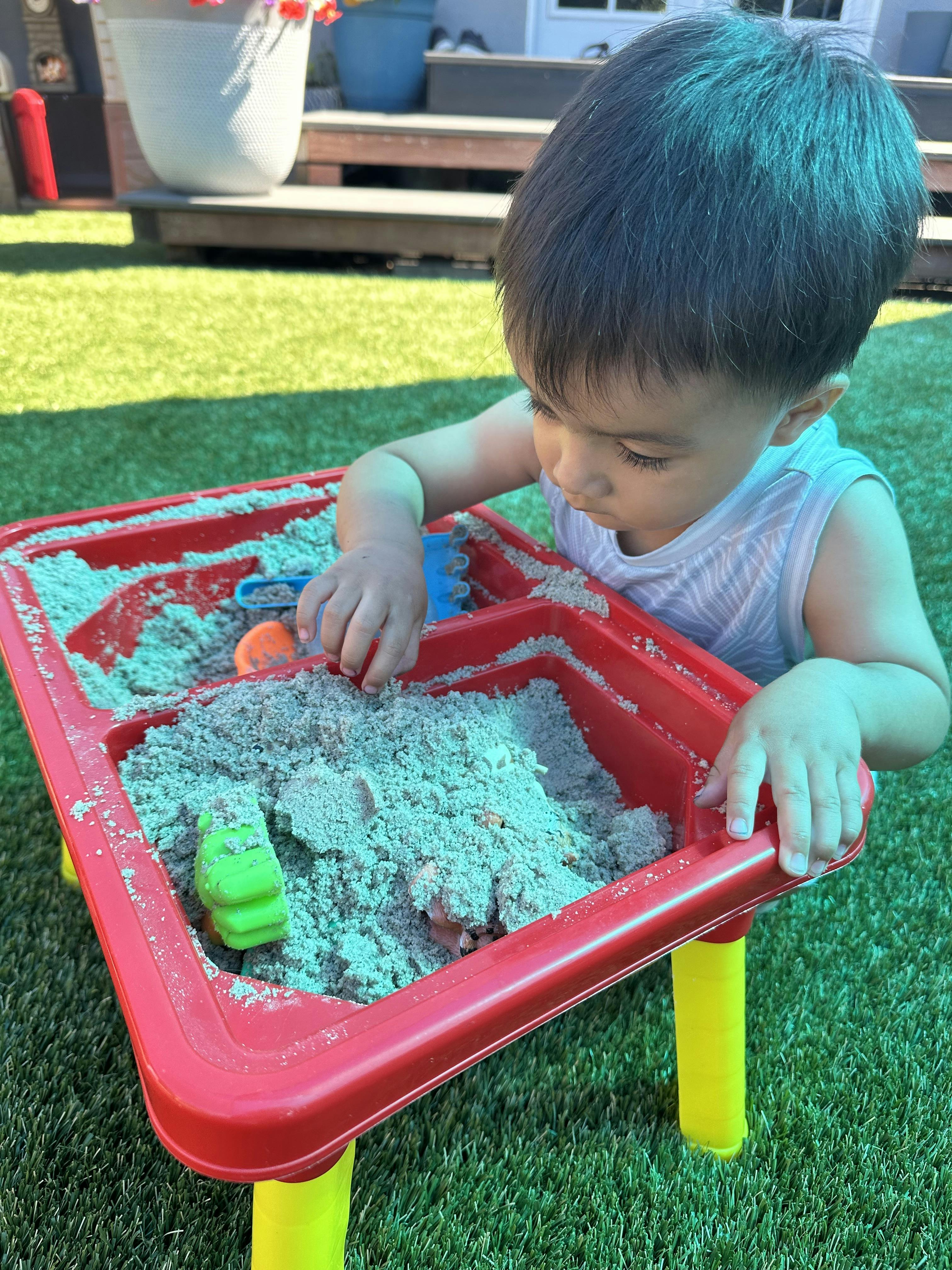 Child playing with sand in a red sensory table outdoors