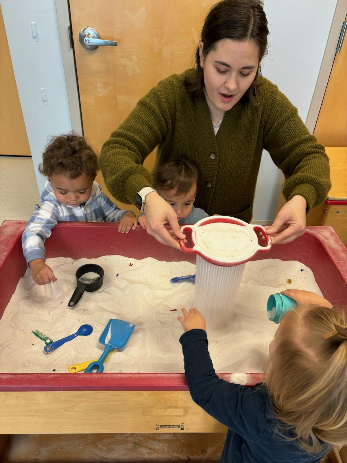 Adult and three children playing in a sand table