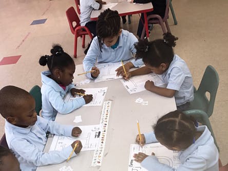 Children writing at a table in a classroom