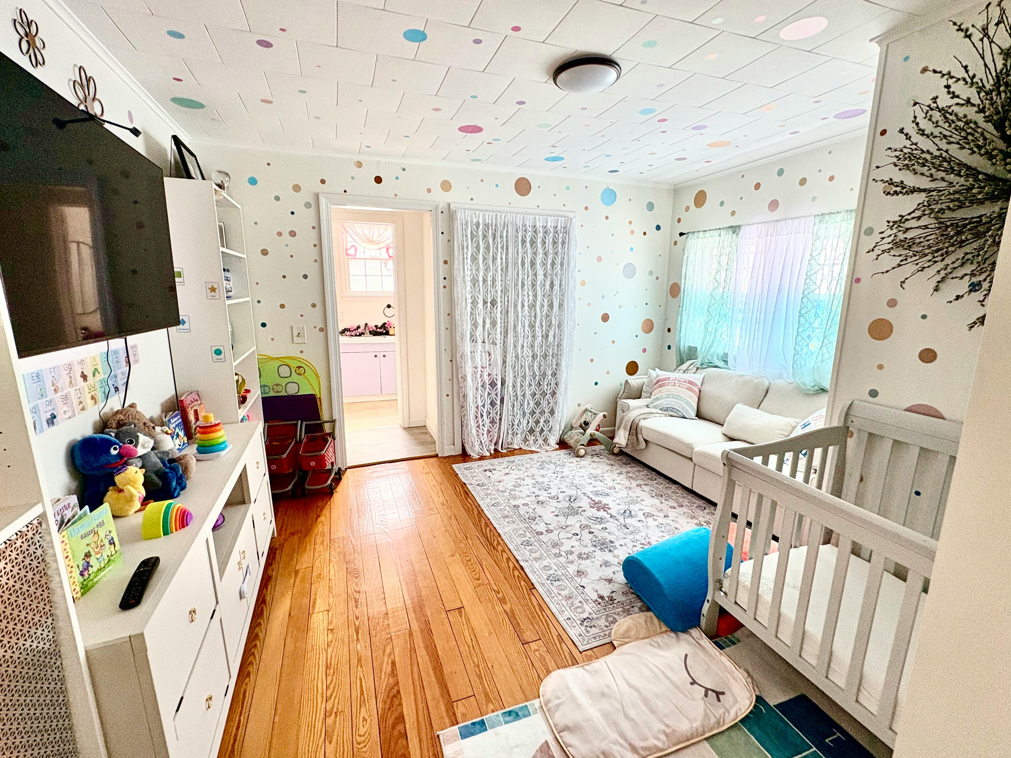 Child's room with a crib, sofa, rug, and walls decorated with colorful dots