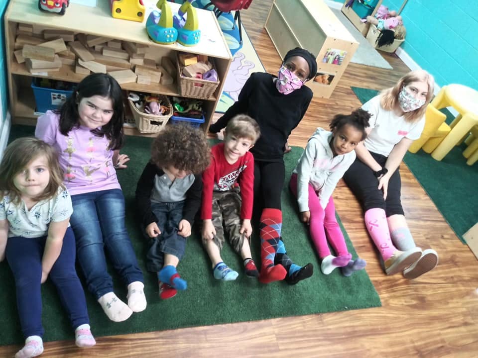 Adults and children sitting on a green rug in a classroom