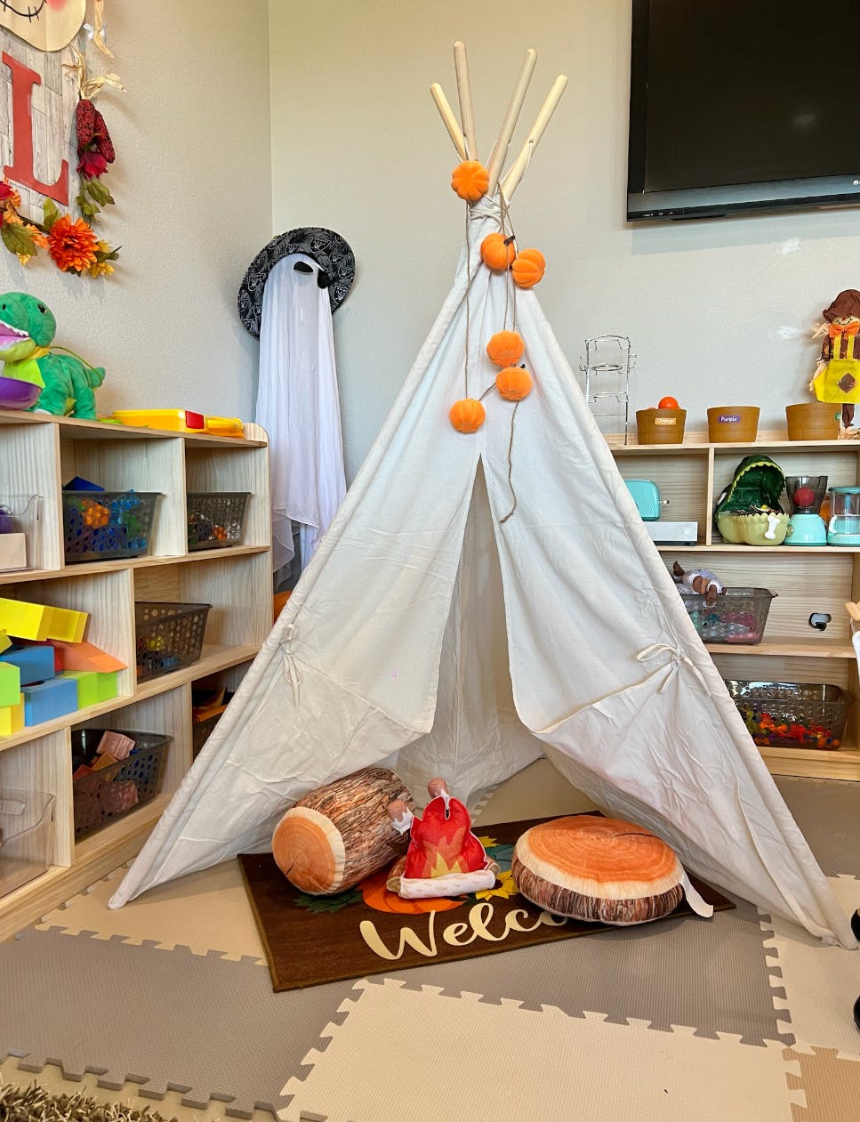 White teepee with orange pom-poms, log pillow, and campfire pillow on a welcome mat