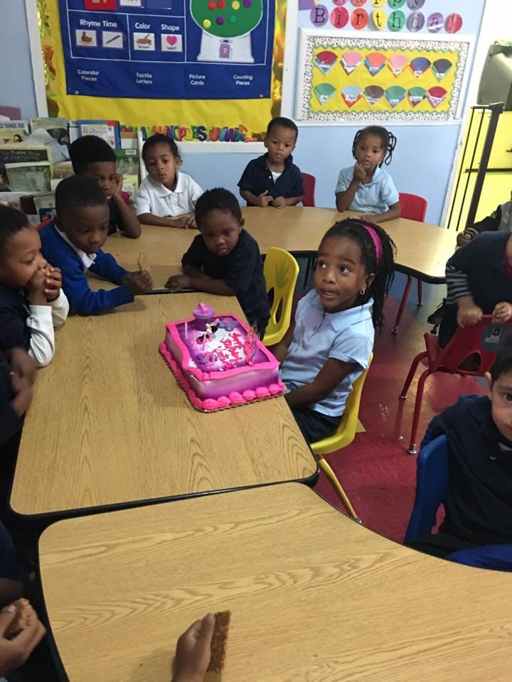 Children sitting at tables with a pink cake in a classroom
