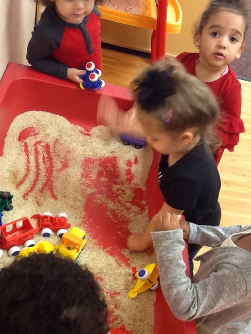 Children playing with toys in a red sensory bin filled with rice