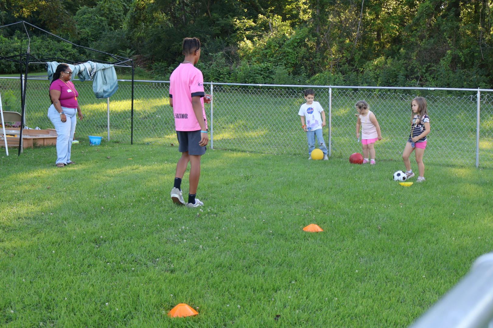 Group of children playing with balls in a grassy field with an adult supervisor