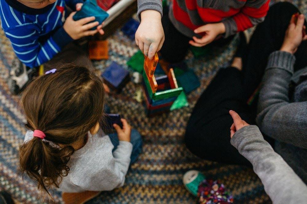 Children playing with magnetic building blocks on a rug