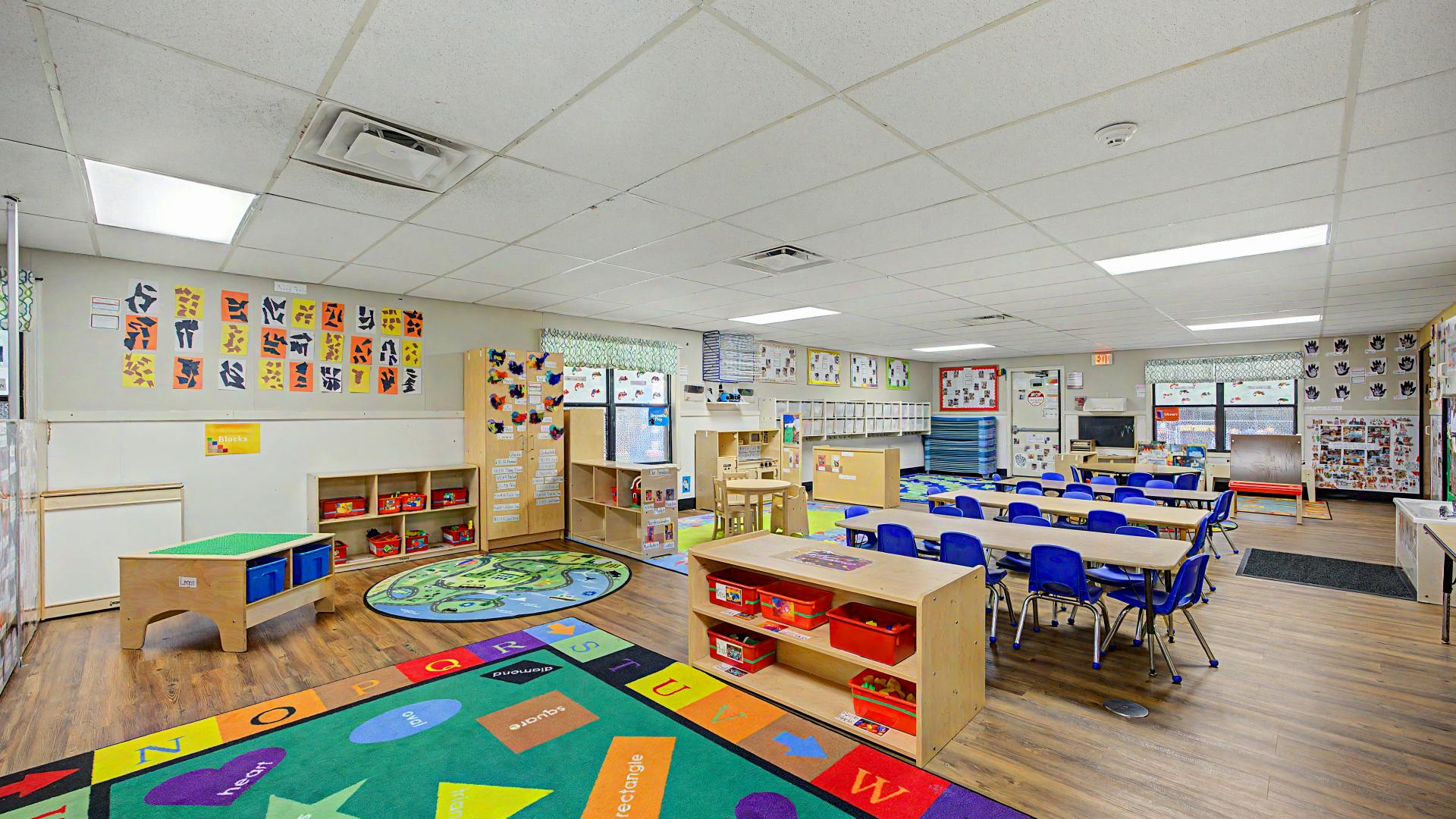 An empty early childhood classroom with colorful carpets, tables, and chairs