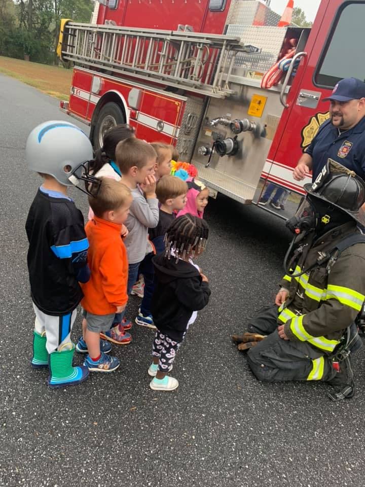 Firefighter in gear kneeling in front of a group of children near a fire truck