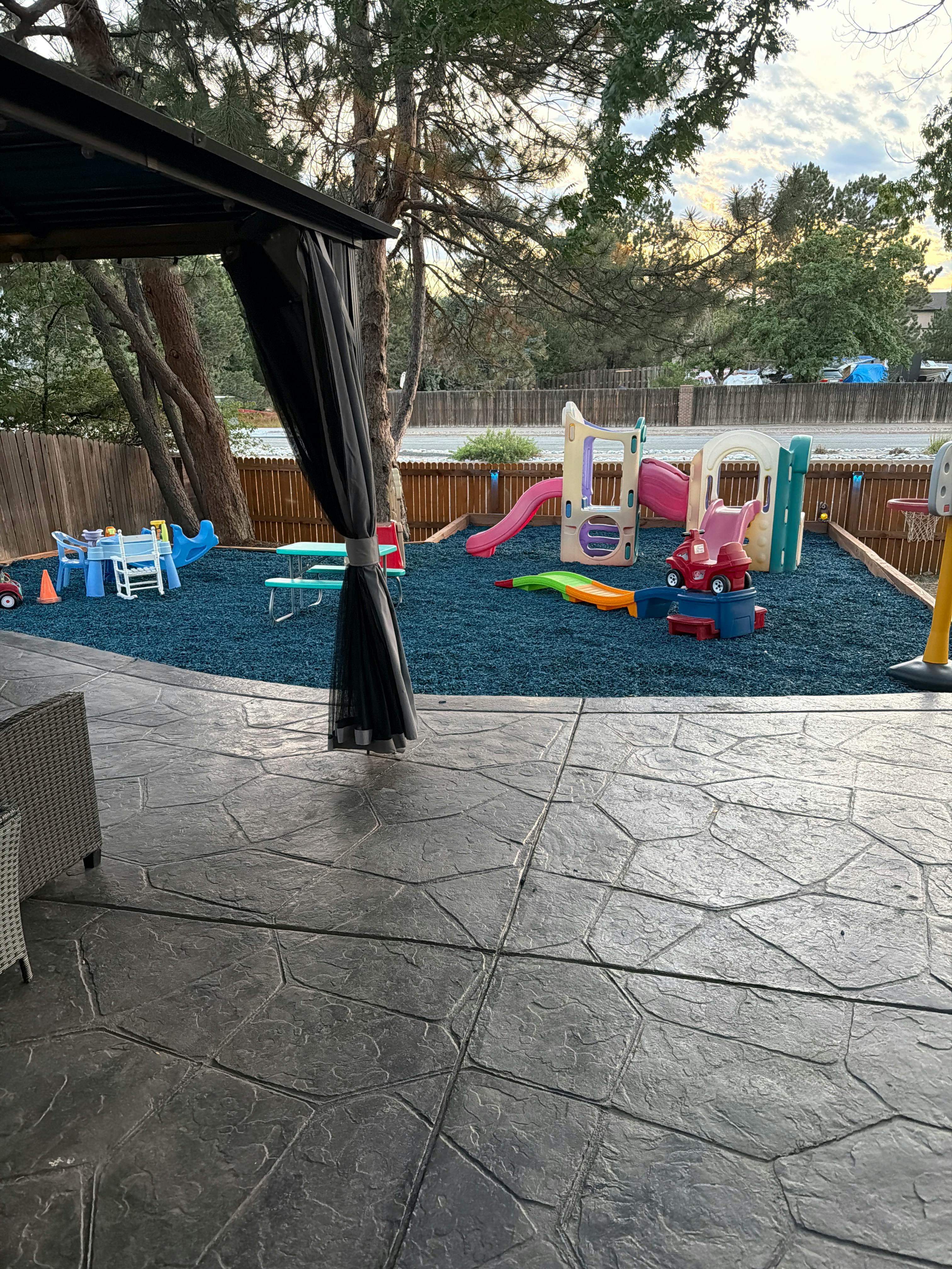 Plastic playground equipment and toys in a backyard with blue rubber surfacing