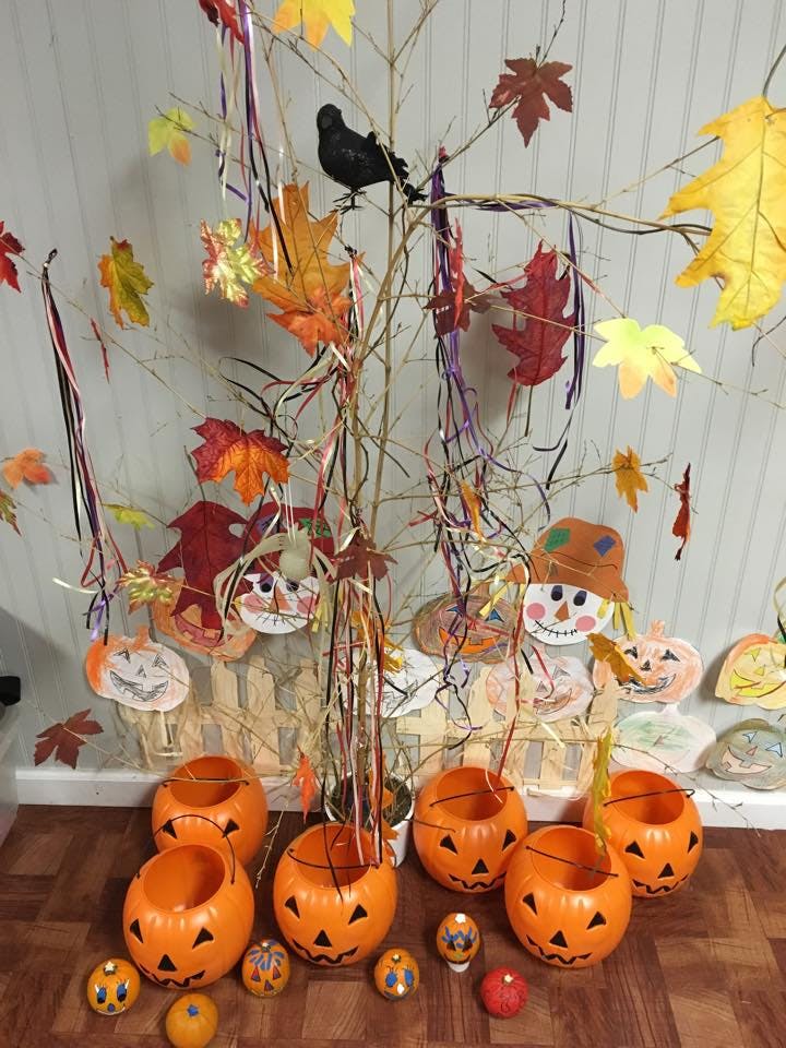 Halloween decorations with a tree, paper leaves, scarecrows, and pumpkin buckets