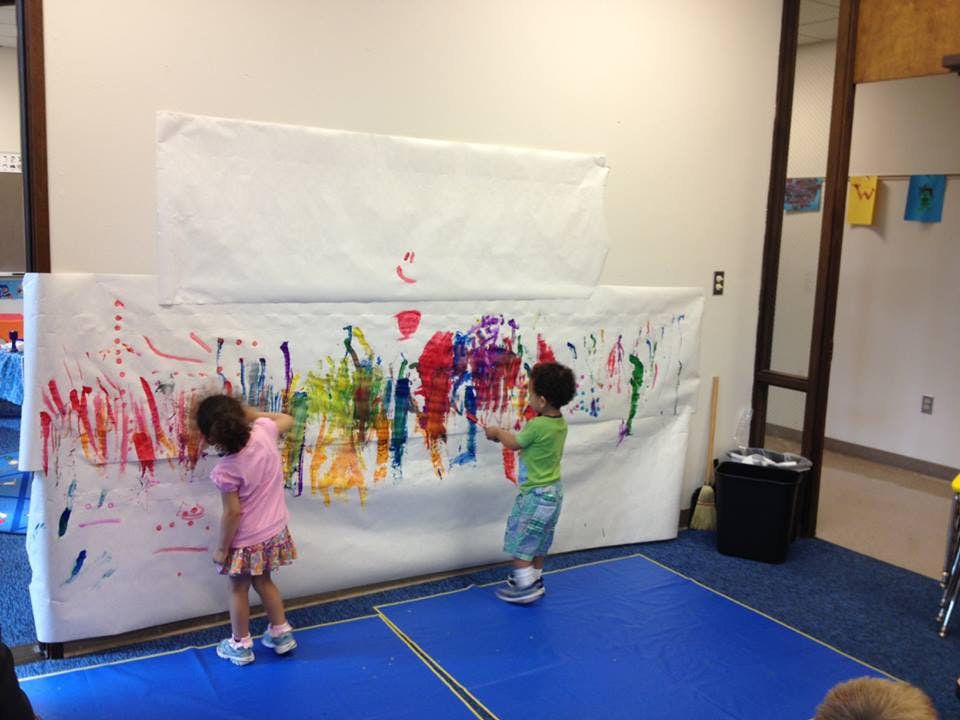 Two children painting on a large white sheet