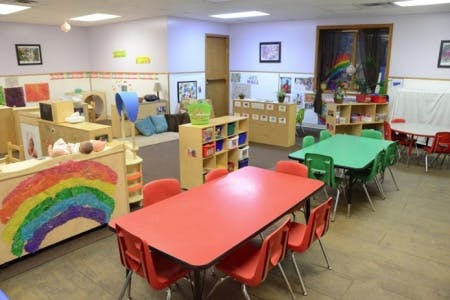 Classroom with small tables and chairs, shelves, and a rainbow drawing