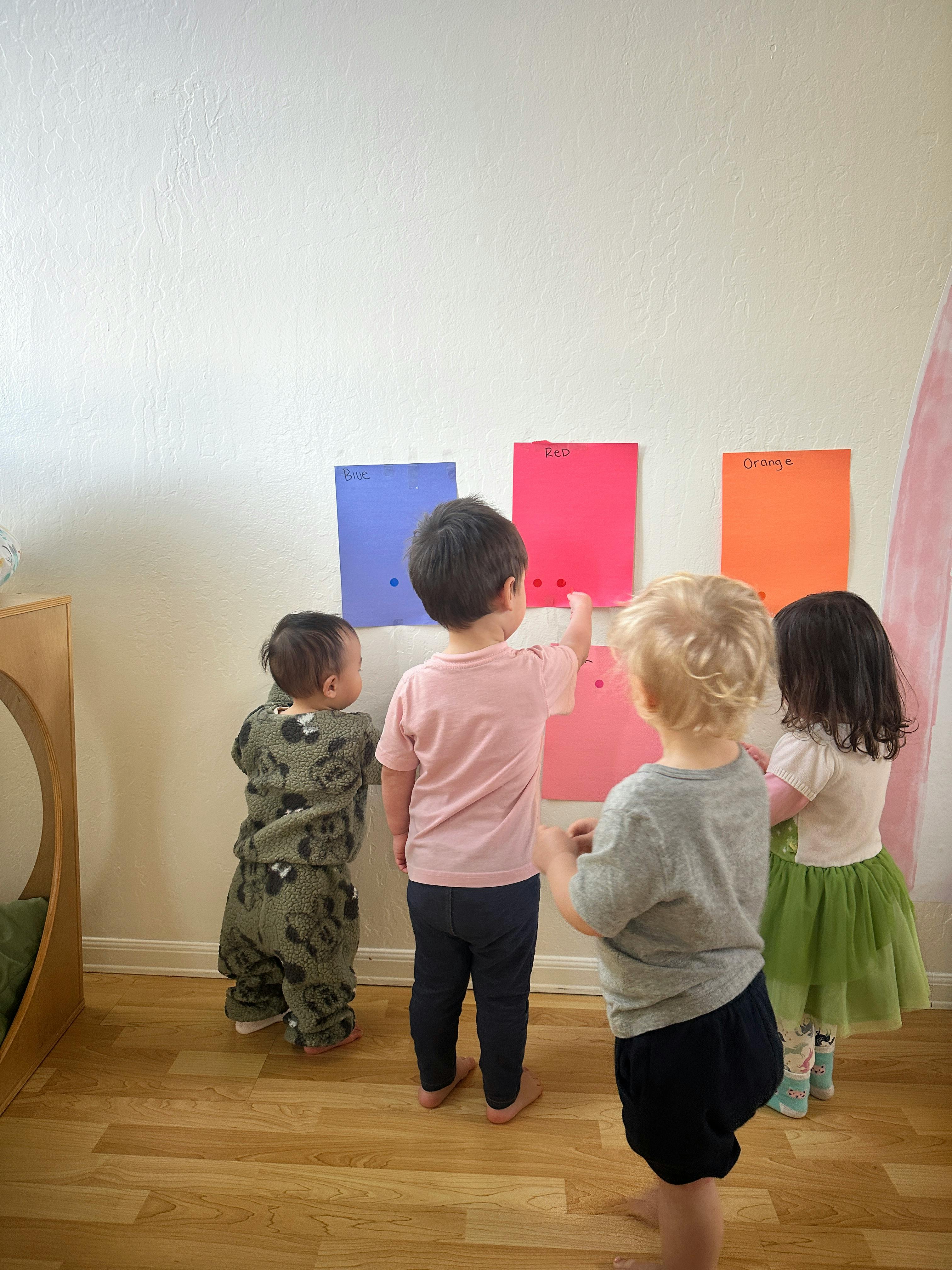 Four children looking at colorful papers on a wall