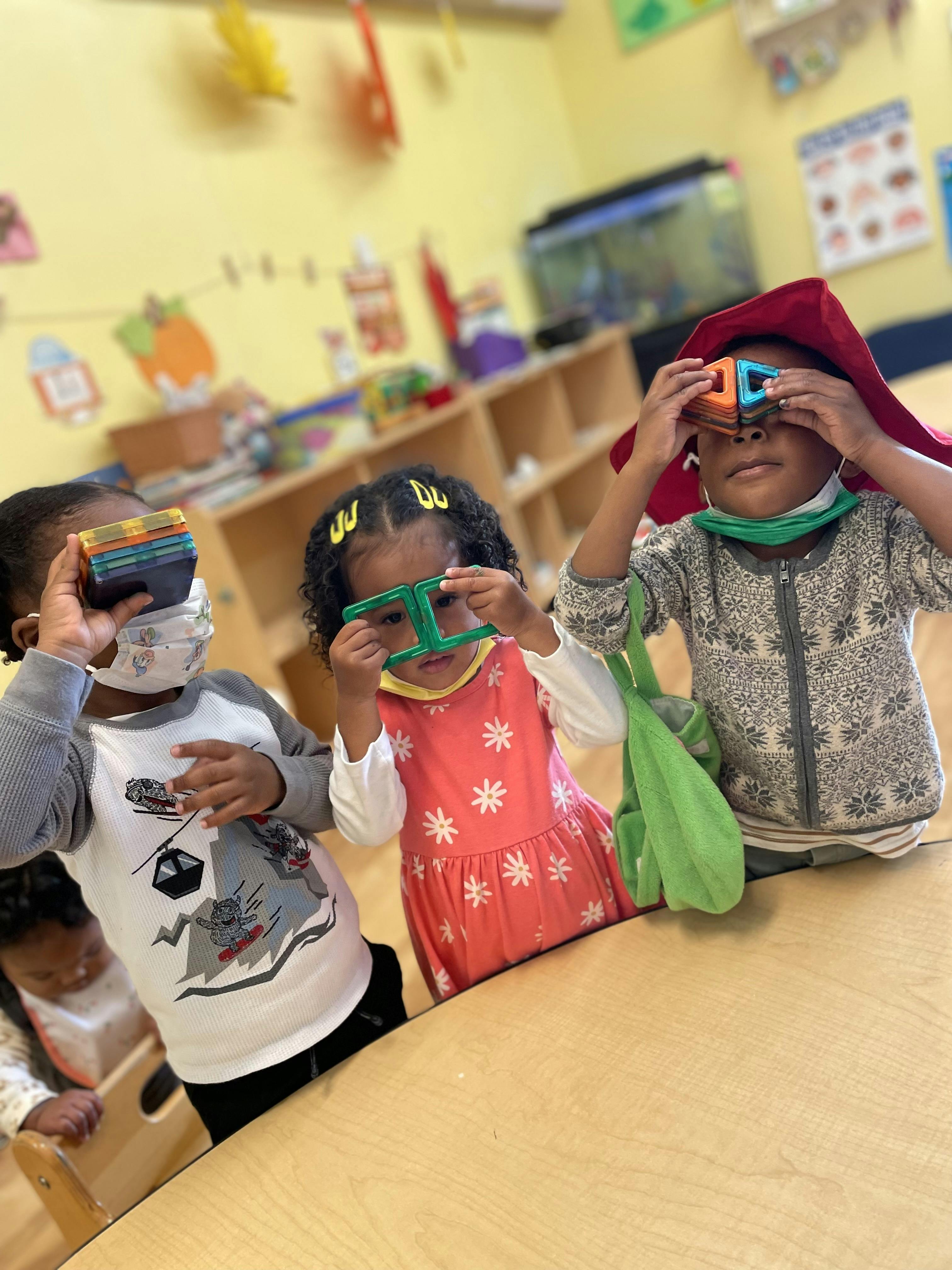 Three children playing with colorful magnetic blocks in a classroom