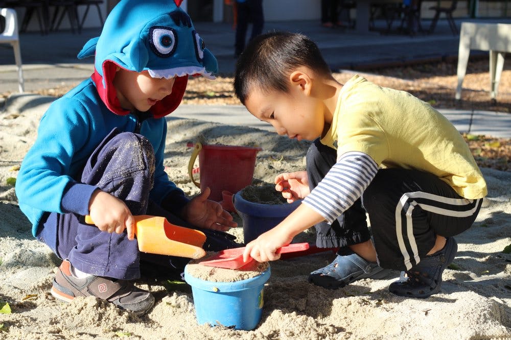 Two children playing in a sandbox with toys