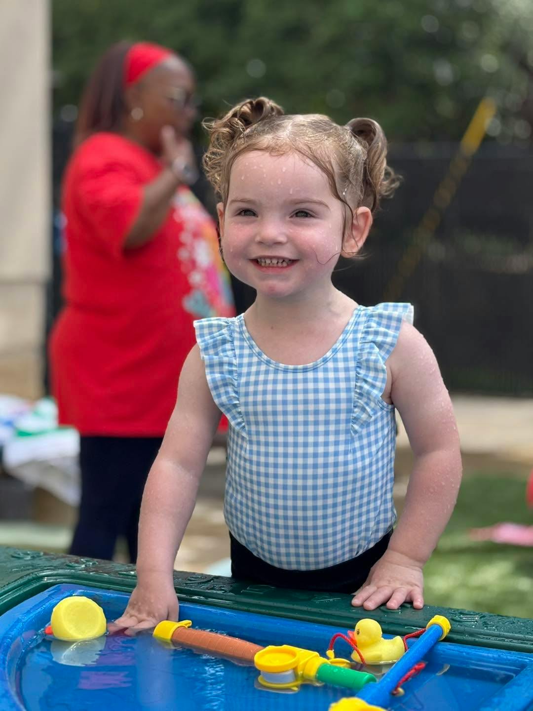 Wet child in a blue checkered swimsuit playing in a water table