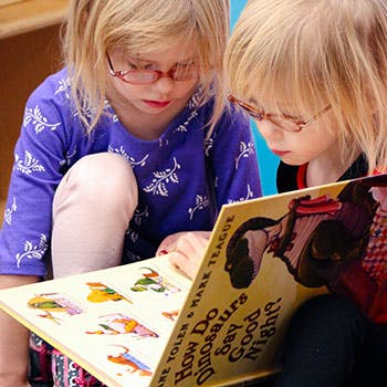 Two children wearing glasses reading a book together