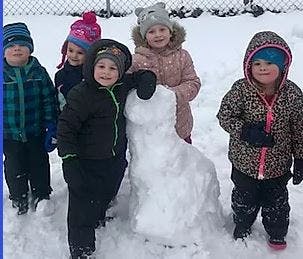 Five children standing around a snowman in the snow