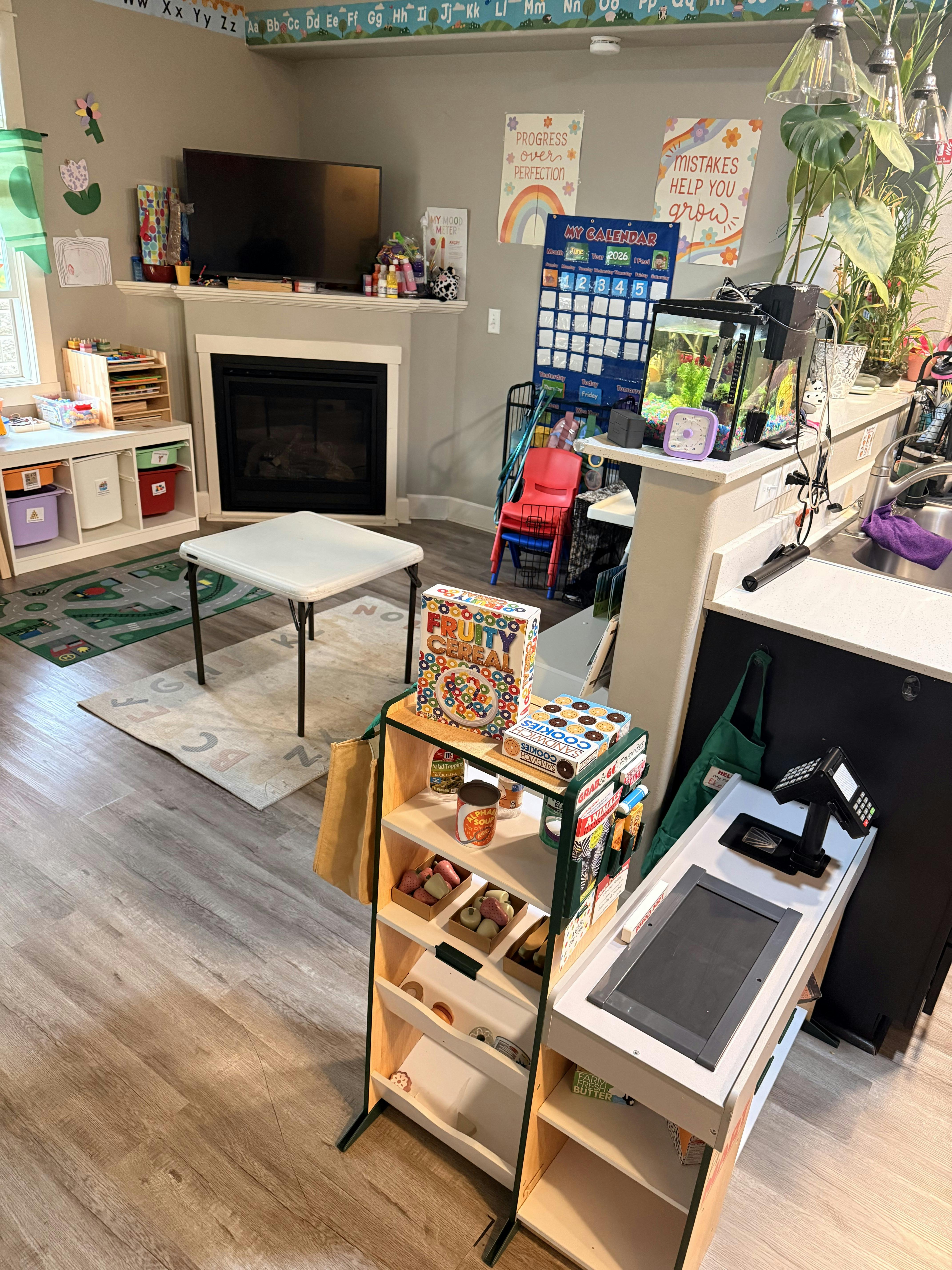 Children's play area with a small table, shelves of toys, and a play register