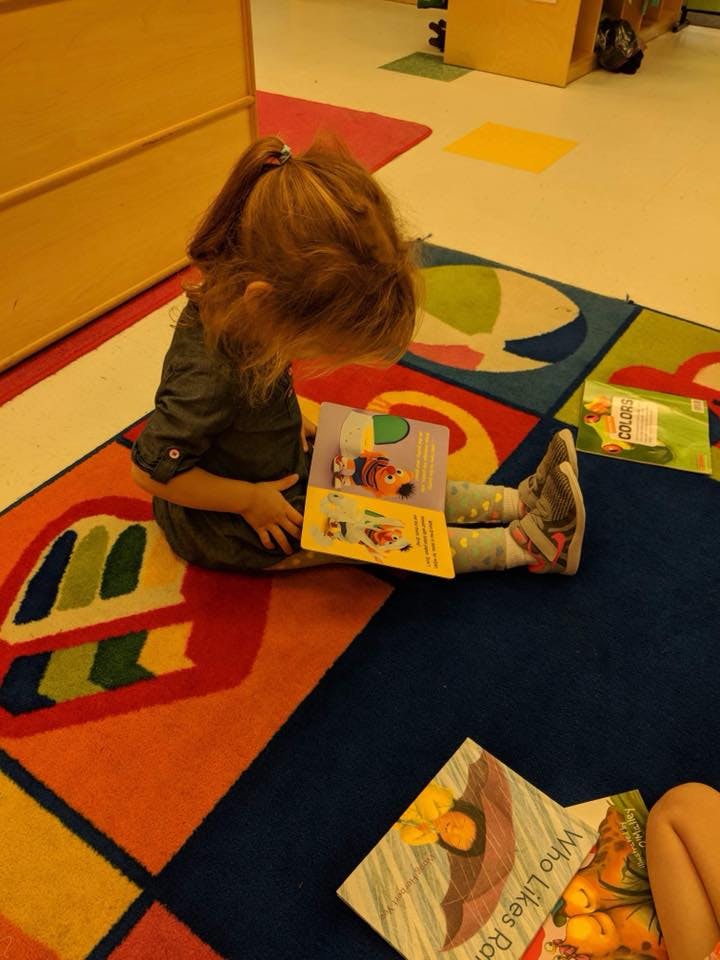 Child sitting on a colorful rug reading a book