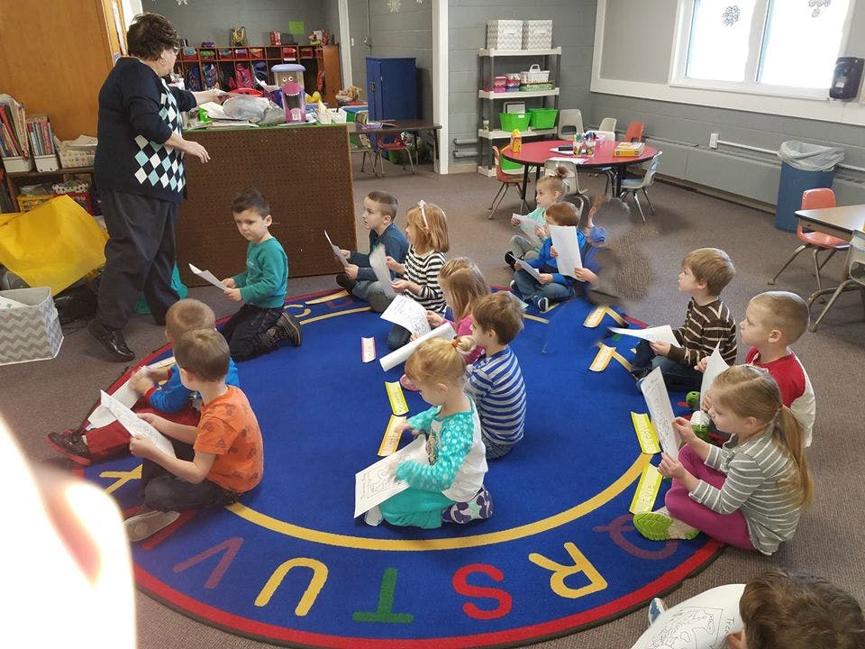 Adult standing in front of children sitting on a rug in a classroom