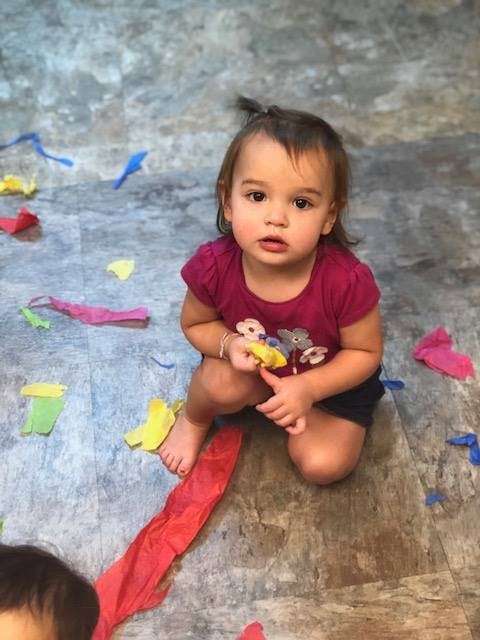 Child kneeling on floor with colorful paper scraps