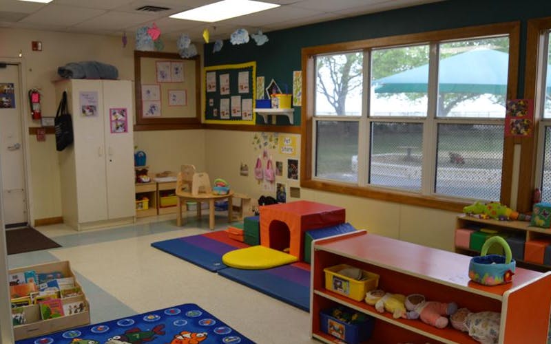 Classroom with play mats, small tables, and windows overlooking a green outdoor space