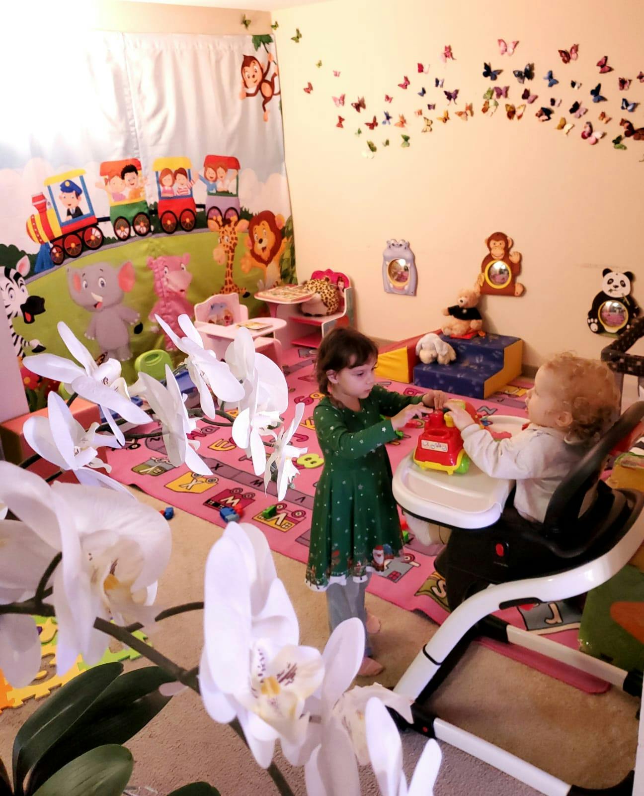 Child standing next to a child in a high chair playing with a toy