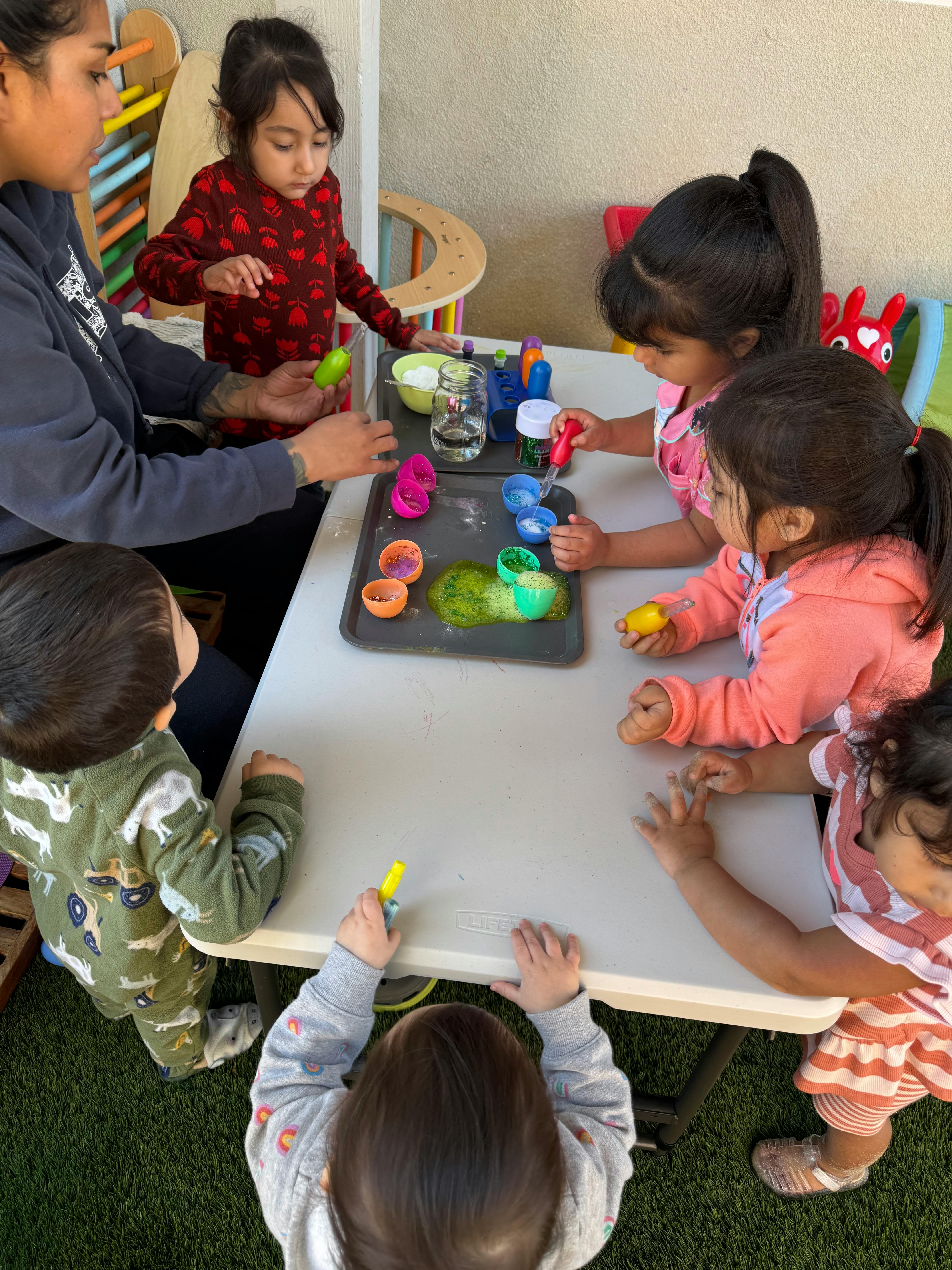 Adult and children playing with colorful items at a table
