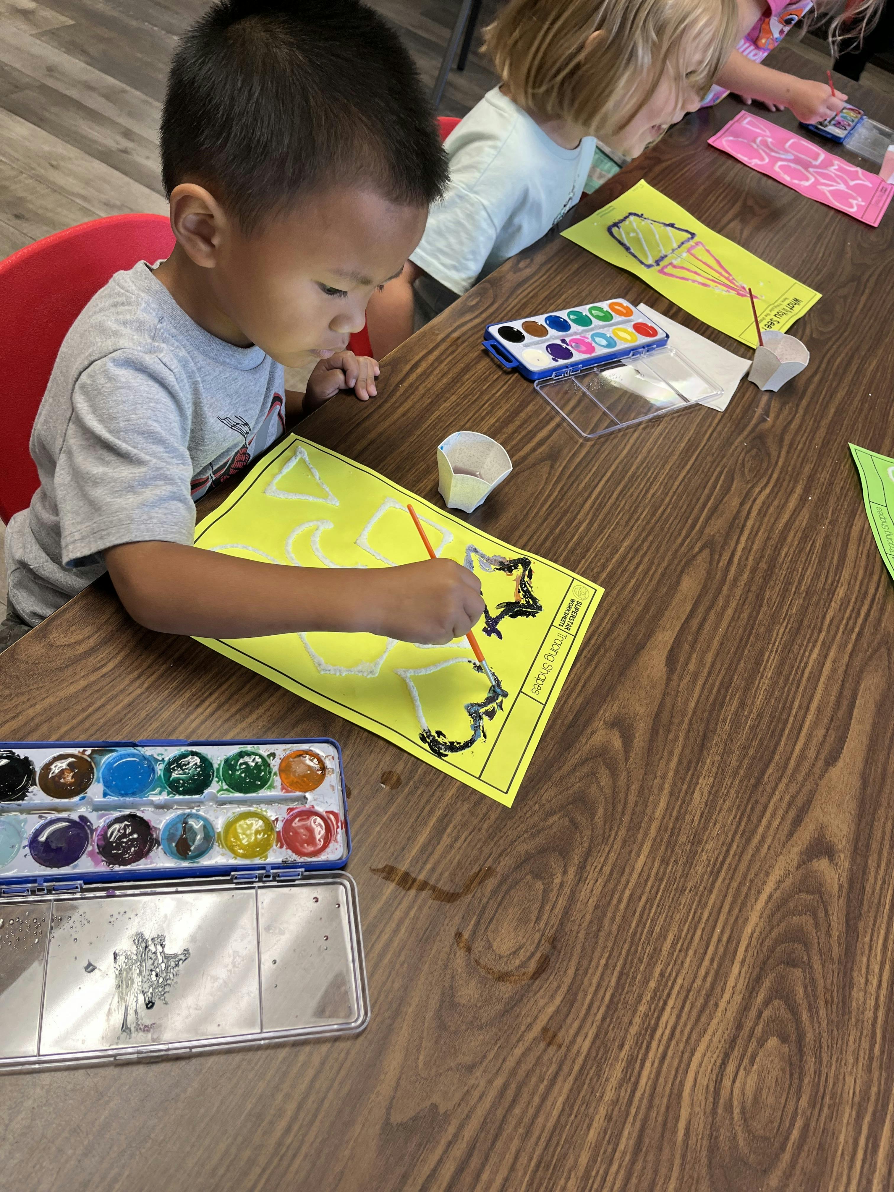 Child painting outlines of shapes on yellow paper