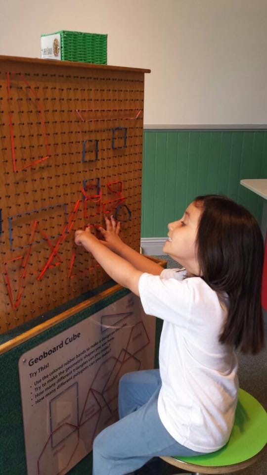 Child sitting and placing rubber bands on a geoboard