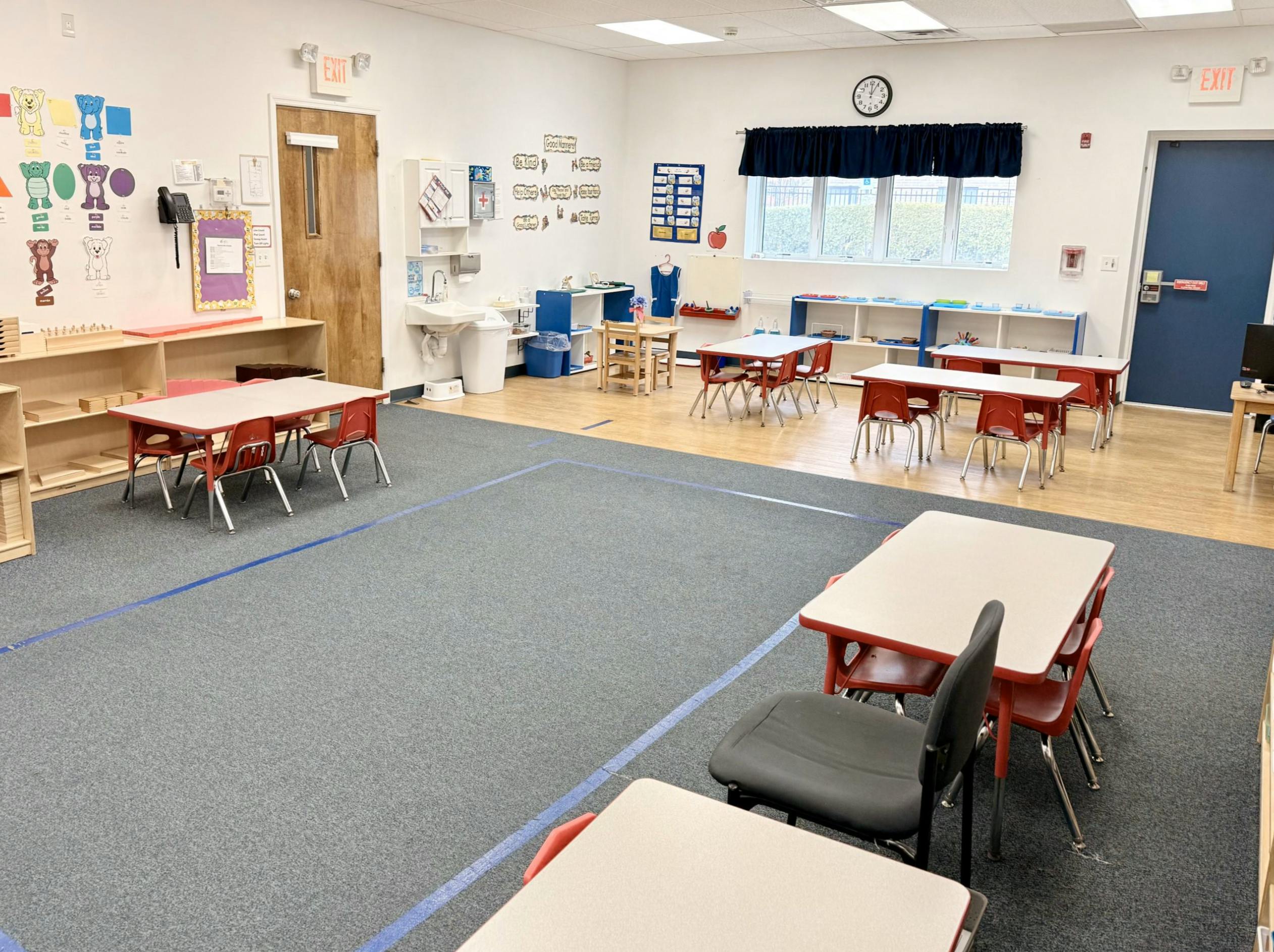 Empty classroom with small tables and chairs, shelves, and a sink area with a sink